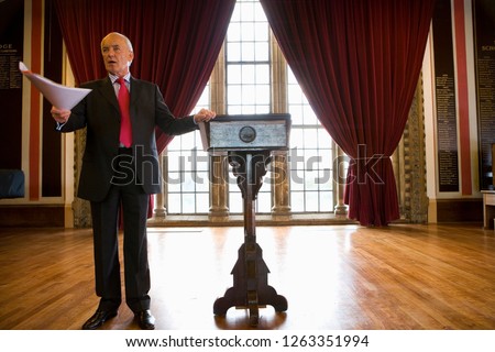 Businessman giving speech by lectern in historic hall
