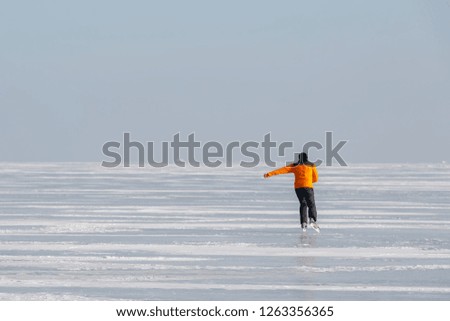 Young man in an orange sweatshirt alone skates on the ice of a frozen sea bay