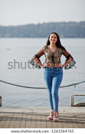 Pretty latino model girl from Ecuador wear on jeans posed against lake.