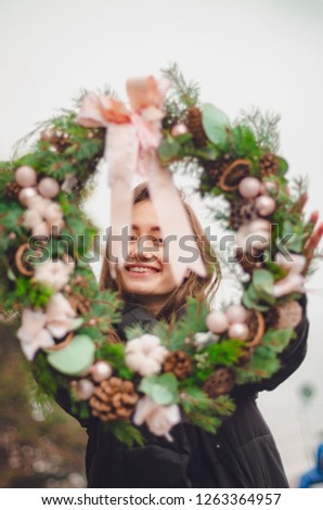 beautiful brunette girl with New Year's mood holds in hands a Christmas wreath decorated with Christmas trees, cones, colored ribbons, flowers, golden bumps and tree toys. selective focus