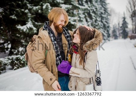 Date of the young couple in the winter. Young Caucasian man with a beard and long hair fooling around kid snow snowballs with a woman, winter games Valentine's Day in the snowy woods.