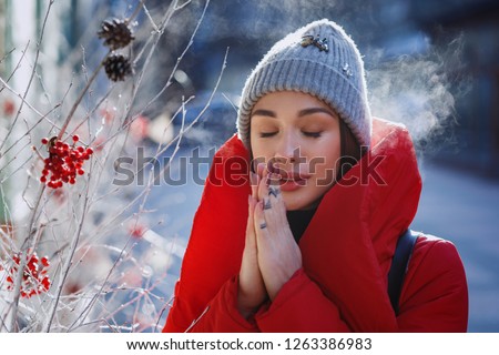 Girl in red winter jacket tries to warm herself standing on the street covered with snow and cold  weather. Christmas, new year and winter holiday concept - Image