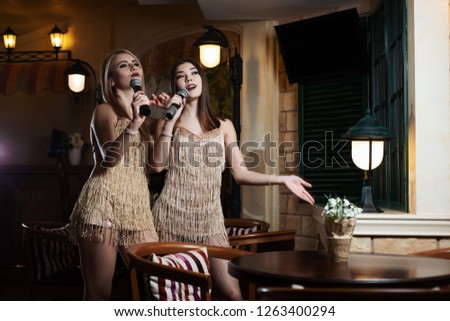 Beautiful women singing karaoke songs in microphones in restaurant