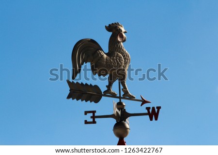 A rooster weather vane set against a cloudy blue sky  Royalty-Free Stock Photo #1263422767