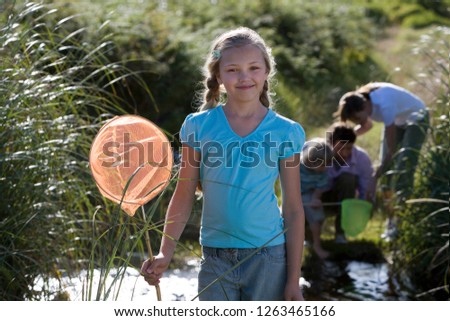 Family by countryside stream fishing with nets at camera