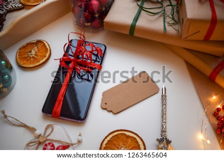 Mobile smartphone tied with a red ribbon surrounded by gifts and other Christmas trifles.