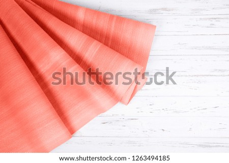 Coral color exercise mat on white wooden background with copy space. Yoga practice, physical workout, pilates or fitness concept.