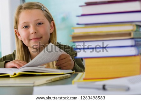 Girl student studying reading textbook at desk in school classroom at camera