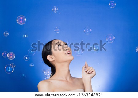 Asian Beautiful Woman black hair blow many bubbles soap in the air over studio lighting blue background, concept Play fun Joyful nice skin, empty copy space for advertising
