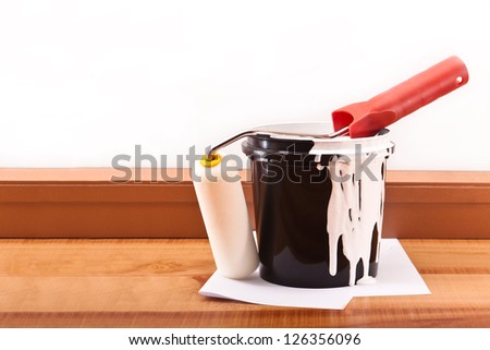 Black bucket of white paint and a roller on the wooden floor
