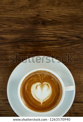 A cup of coffee with heart pattern in a white cup on rustic wooden background with beautiful latte art