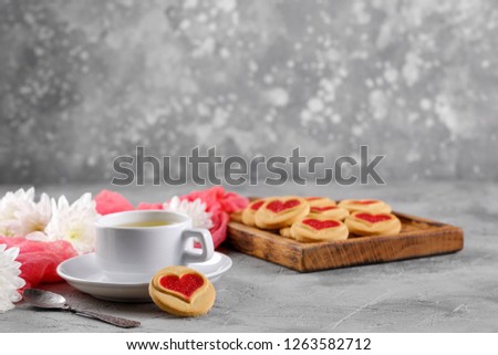 White cup and cookies with hearts on a gray background. Beautiful still life, the mood of Valentine's Day. Side view. Space under the text.