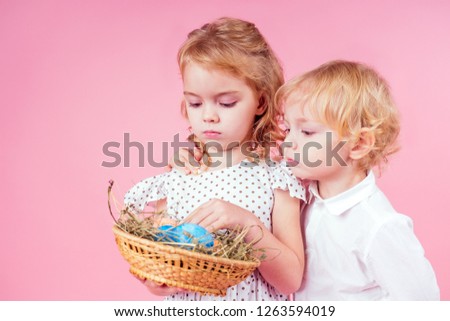 two little blonde child with a chick cock easter in studio pink background.beautiful boy and girl kids celebrating Easter Holiday with pets, painted eggs in wicker basket.dream birthday present