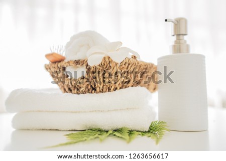 Ceramic soap, shampoo bottles and white cotton towels with green plant on white counter table inside a bright bathroom background 