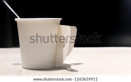 A white coffee cup is placed on a table with a black background.