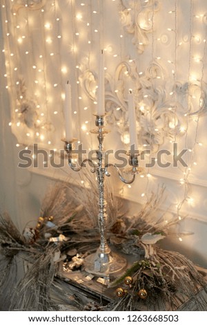 Three-horn candlestick, garland. White and silver decor. The new year atmosphere. Christmas decoration at home.