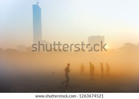 Beautiful image of sunrise at Kolkata maidan in a foggy winter morning. Sunrises at the horizon above city skyscappers and football players getting ready for a match in foreground.