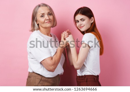 A young girl and an elderly woman joined hands on a pink background                               
