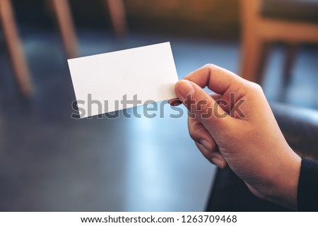 A hand holding white empty business card with blurred background