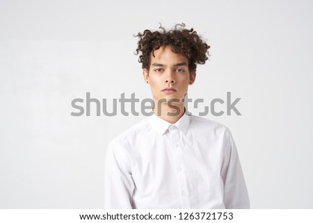 Curly handsome man in a white shirt on a light background             