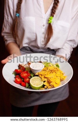 A waitress in a white shirt is holding a delicious salad.