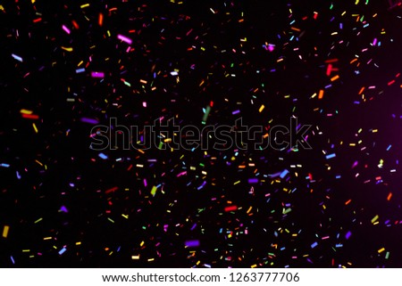 Thousands of confetti fired on air during a festival at night. Image ideal for backgrounds. Multicolor are the confetti in the picture. The sky as background is black. Warm tonality