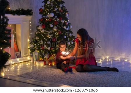 mother and son celebrate the new year at a Christmas tree with gifts Garland lights