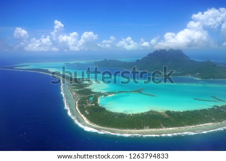 Aerial panoramic landscape view of the island of Bora Bora in French Polynesia with the Mont Otemanu mountain surrounded by a turquoise lagoon, motu atolls, reef barrier, and the South Pacific Ocean Royalty-Free Stock Photo #1263794833