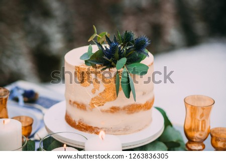 The beige cake is decorated with flowers, standing on the table near to the candles