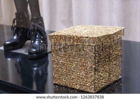 Golden shiny gift box next to black women's boots in a shoe store display case. Shallow depth of field and copy space. The concept of gift shopping or hotel discounts for the new year or birthday.