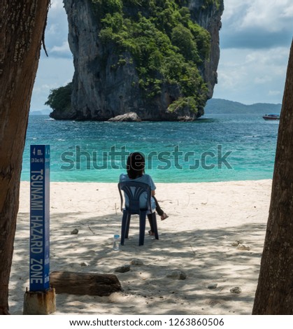 woman sitting on chair on beach in front of Sunami Hazard sign