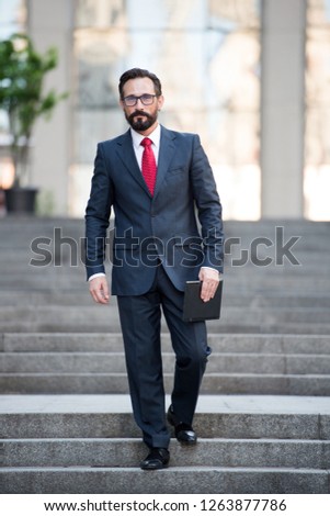 Full length of attractive middle aged businessman keeping digital tablet in hand while descending city stairs and expressing calmness