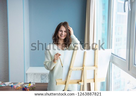 young pretty girl paints a picture in front of a large window