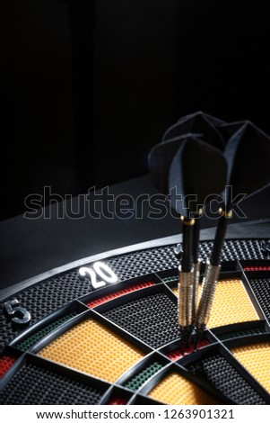 Close up of three darts in triple 20 of dartboard.Ton 80. Black Darts