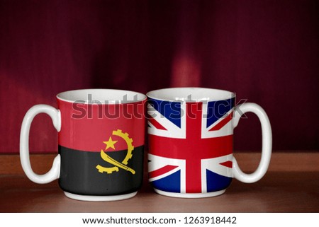 United Kingdom and Angola flag on two cups with blurry background