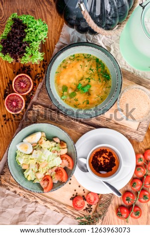 Cup of black tea, caesar salad and chicken broth in gray plates on wooden boards in rustic composition. close-up. top view