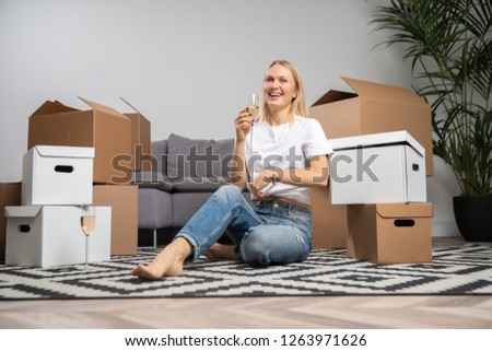 Photo of happy woman with champagne glass sitting on floor among cardboard boxes
