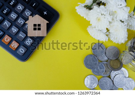 Wooden house model, calculator and coins on light yellow background. Property investment, Home finance concept. Copy space for text.