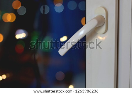 Blurred bokeh bright multi-colored city night lights window view and white handle to open the window with free copy space for text