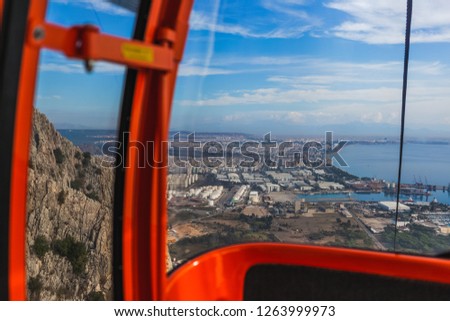 Inside of red cabin of cableway on picturesque mountains. Cabin driving over huge mountains. Beautiful view at city in distance. Horizontal color photography.