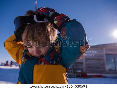 little boy having a problem with ski goggles during winter vacation on beautiful alpine mountain resort