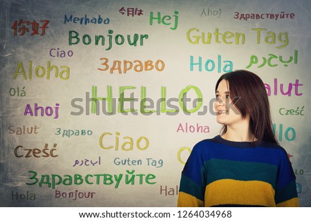 Pretty girl in front of a blackboard written with the word hello in different languages and colors. Opportunity for learning many languages for students.