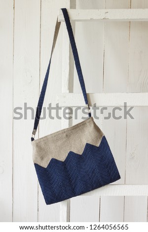 Crossbody bag hangs on a white wooden ladder. Linen bag. Knitted blue decor. Light background Royalty-Free Stock Photo #1264056565