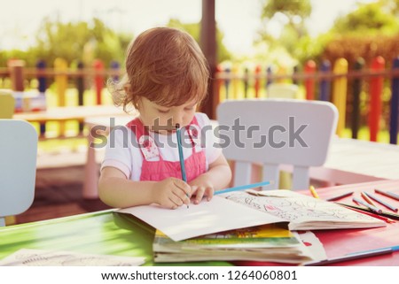 cute little girl cheerfully spending time using pencil crayons while drawing a colorful pictures in the outside playschool