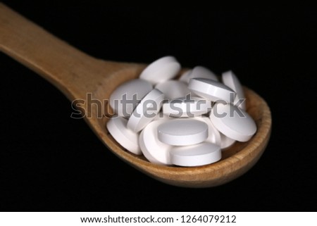 Wooden spoon with vitamin tablets against a black background
