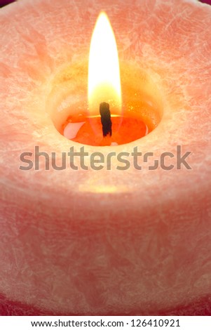 Close up to the flame of a red candle burning on a red background.