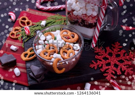 Hot chocolate with marshmallows and pretzels in a cup and a dry mix for preparing the drink in a glass jar