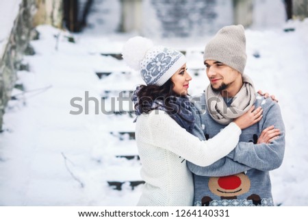 man and girl in sweaters hugging in the park in winter. young couple in love having fun on a winter walk