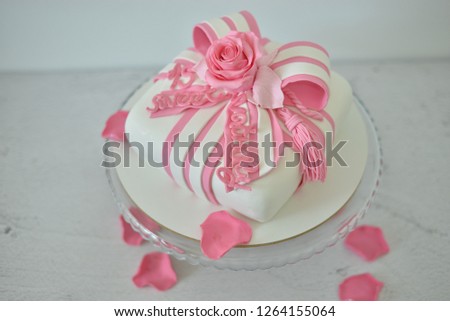 White cake on marble background, decorated with pink rose and a bow with rose leafs 