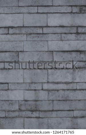 Close up outdoor view of a grey wall made of rectangular stone bricks. Gray textured surface with parallel lines and geometric shapes. Picture of a facade with dark traces. 